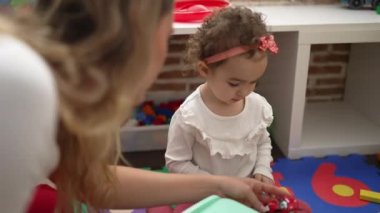 Öğretmen ve bebek arabalarla oynuyor. Anaokulunda yerde oturuyor.