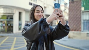 Genç, güzel, İspanyol bir kadın gülümsüyor. Akıllı telefonuyla caddede kendine güvenen bir video kaydediyor.