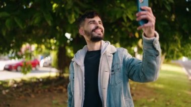 Genç İspanyol adam gülümsüyor. Parkta kendine güvenen bir video çağrısı var.