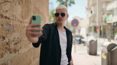 Kafkasyalı genç adam gülümsüyor. Sokakta akıllı telefonun yanında özçekim yapıyor.