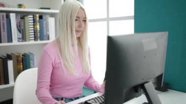 Young blonde woman student using computer studying at library university