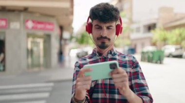 Young hispanic man smiling confident playing video game at street