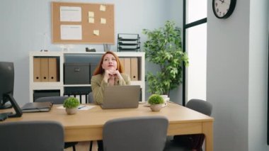 Genç, kızıl saçlı, iş kadını. Ofiste dizüstü bilgisayar kullanıyor.