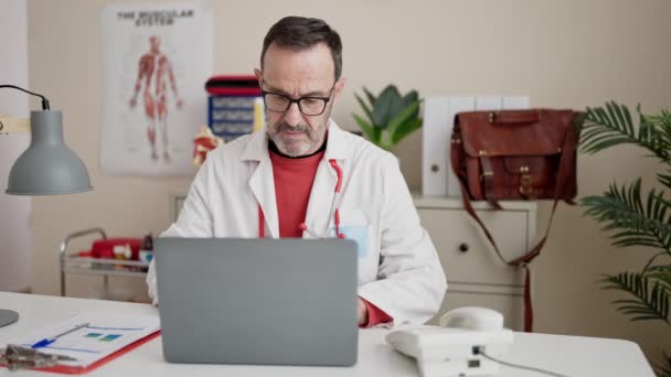 Middle Age Man Doctor Using Laptop Working Clinic — Vídeo de Stock