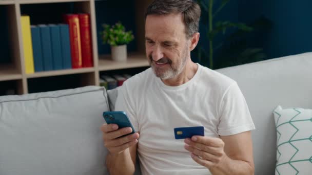 自宅でソファに座っているスマートフォンやクレジットカードを使用して中世の男 — ストック動画