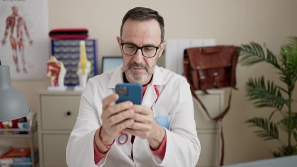 Middle Age Man Doctor Using Smartphone Working Clinic — Stockvideo