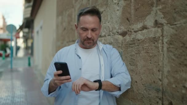 Νεαρός Καυκάσιος Άνδρας Που Χρησιμοποιεί Smartphone Ψάχνει Ρολόι Στο Δρόμο — Αρχείο Βίντεο