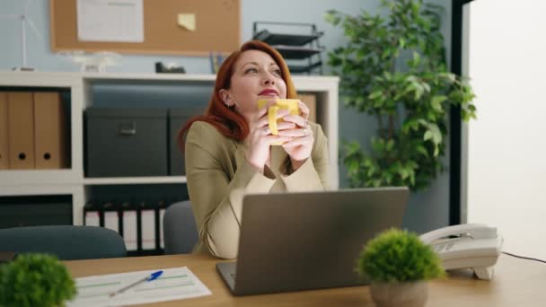 Νεαρή Κοκκινομάλλα Επιχειρηματίας Χρησιμοποιώντας Φορητό Υπολογιστή Πίνοντας Καφέ Στο Γραφείο — Αρχείο Βίντεο