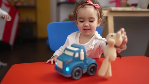 愛らしいですCaucasian女の子遊びますとともにトラックおもちゃ座っています上のテーブルの上に幼稚園 — ストック動画