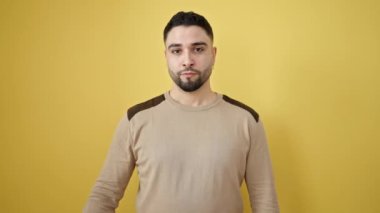 İzole edilmiş sarı arka planda öfkeli bir ifadeyle duran genç bir Arap.