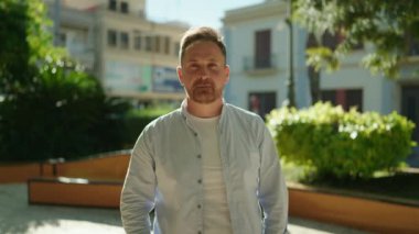 Parkta kendine güvenen beyaz bir adam gülümsüyor.