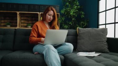 Young redhead woman with serious expression working at home