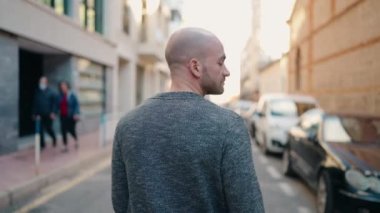 Genç kel adam sokakta yürürken kendinden emin gülümsüyor