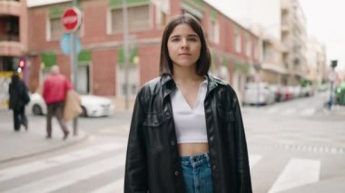 Genç İspanyol kadın gülümsüyor. Kollarını kavuşturup caddede duruyor.