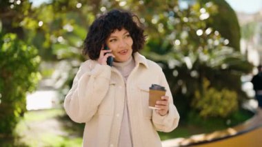 Genç İspanyol kadın akıllı telefondan konuşuyor parkta kahve içiyor.