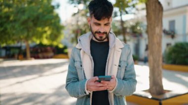 Parkta akıllı telefon kullanarak gülümseyen İspanyol genç adam.