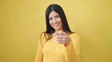 Genç, güzel, İspanyol bir kadın gülümsüyor. Telefon hareketleriyle kendine güveniyor. Sarı arka planı elden ele gezdiriyor.