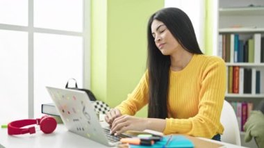 Young beautiful hispanic woman student using computer stressed at library university