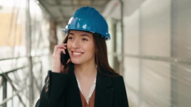 Young hispanic woman architect talking on the smartphone at street