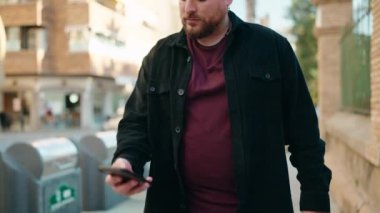 Young plus size man smiling confident using smartphone at street