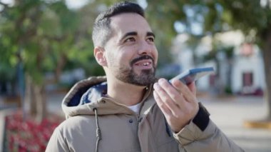 Genç İspanyol adam gülümsüyor. Parkta akıllı telefonla sesli mesaj yolluyor.