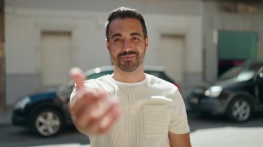 Young hispanic man smiling confident doing coming gesture with hand at street