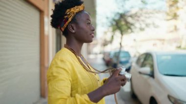 Young african american woman smiling confident using vintage camera at street