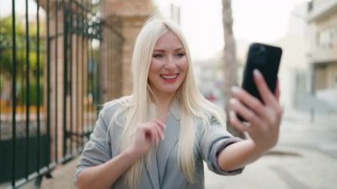 Genç sarışın kadın yönetici caddede video görüşmesi yapıyor.