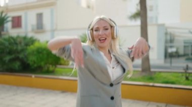 Genç sarışın kadın yönetici parkta müzik dinliyor ve dans ediyor.
