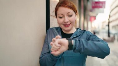 Genç kızıl saçlı kadın spor giyer Sokakta kronometreye bakar