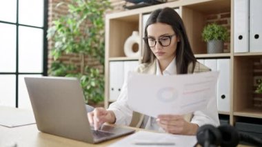 Young beautiful hispanic woman business worker using laptop reading document at office