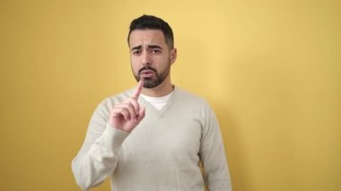 Genç İspanyol adam, izole edilmiş sarı arka planda negatif jest yapıyor.
