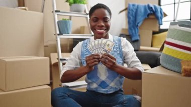 Afro-Amerikalı kadın gülümsüyor. Yeni evinde dolarları elinde tutuyor.