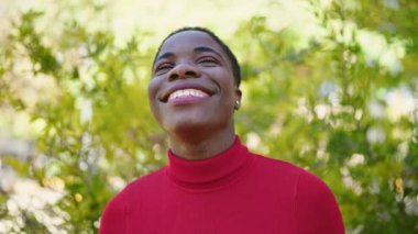 Afro-Amerikalı kadın parkta kendinden emin bir şekilde gülümsüyor.