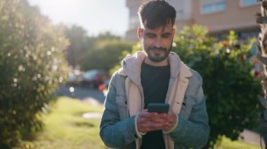 Parkta akıllı telefon kullanarak gülümseyen İspanyol genç adam.