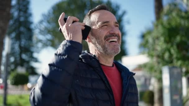 中年男性笑顔自信に満ちたリスニング音声メッセージによってスマートフォンによって公園 — ストック動画