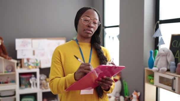 幼稚園のクリップボードに書いて教師として働いているアフリカの女性 — ストック動画