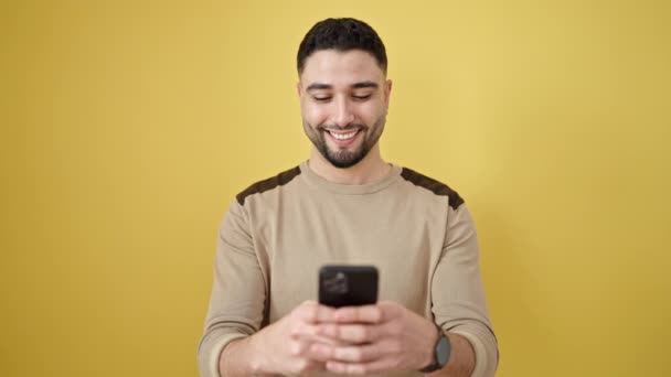 Młody Arabski Człowiek Uśmiechnięty Pewnie Pomocą Smartfona Odizolowanym Żółtym Tle — Wideo stockowe