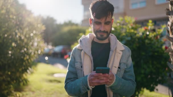 Молодий Іспаномовний Чоловік Посміхається Впевнено Використовуючи Смартфон Парку — стокове відео