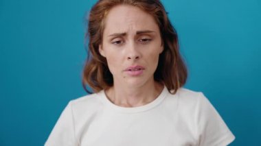 Genç, güzel, İspanyol bir kadın baş ağrısı çekiyor ve mavi arka planda ağlıyor.