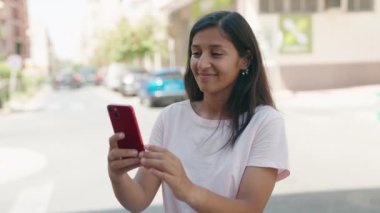 Genç ve güzel İspanyol kadın gülümsüyor. Kendine güveni tam. Sokakta akıllı telefonun yanında selfie çekiyor. 