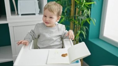 Beyaz çocuk yemek odasında yüksek sandalyede oturmuş kurabiye yiyor.