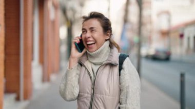 Orta yaşlı bir kadın gülümsüyor. Sokakta akıllı telefondan konuşuyor.