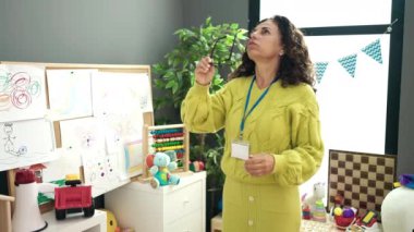 Middle age hispanic woman preschool teacher stressed standing at kindergarten