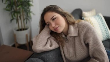 Genç, güzel, İspanyol bir kadın. Elleri başının üstünde, evdeki kanepede oturuyor.