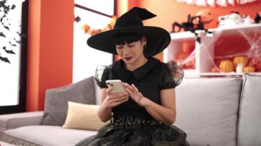 Young chinese woman wearing witch costume using smartphone at home