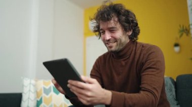Genç İspanyol adam evdeki koltukta otururken dokunmatik ped kullanıyor.