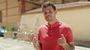 Young hispanic man smiling confident doing spend money gesture at street