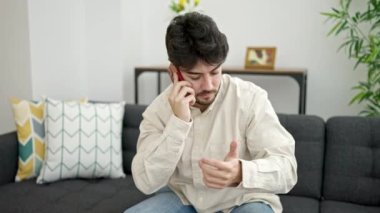 Genç İspanyol adam akıllı telefondan konuşuyor. Evdeki kanepede oturuyor.