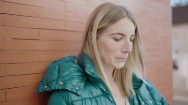 Young blonde woman standing with serious expression thinking at street